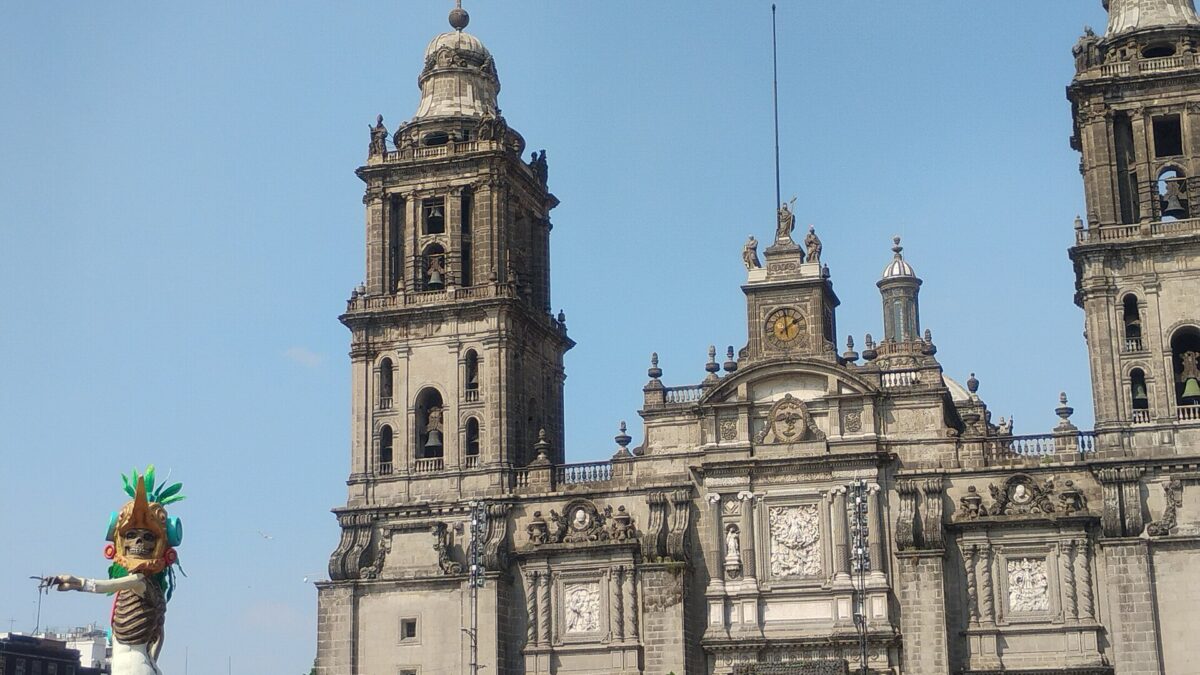 Torre de la Catedral Metropolitana en el Zócalo de la Ciudad de México, con una figura de catrina de una ofrenda de Día de Muertos a la izquierda